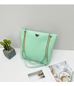 Detalle del bolso tote tejido verde menta con cadena dorada y placa Lucky For You