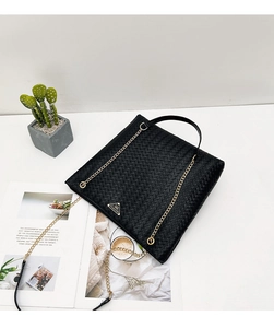 Detalle del bolso tote trenzado negro con cadena dorada y placa metálica