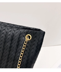 Detalle del bolso tote trenzado negro con diseño tejido y correa de cadena dorada