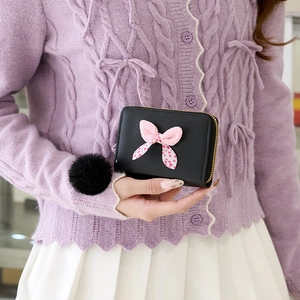 Mini black polka dot bow wallet with fur ball pendant held by a model in casual wear