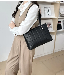 Detail of black quilted tote bag with golden rivets shown in an indoor lifestyle setting