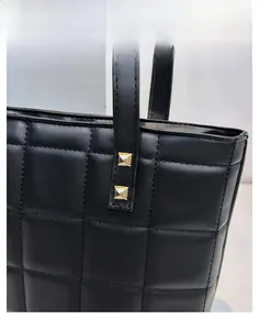 Close-up of black plaid quilted tote bag fabric with gold square rivets and shiny texture