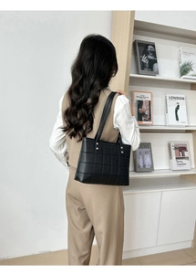 Detail of black quilted tote bag featuring golden hardware and leather shoulder straps