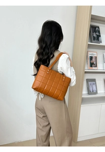 Detail of caramel quilted tote bag with square stitching and gold rivet hardware on shoulder strap