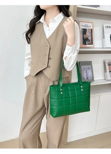 Detail of green quilted tote bag with gold rivets and wide strap shown in lifestyle setting