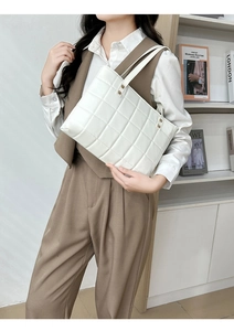Detail view of a white quilted tote bag worn by a model in a minimalist setting