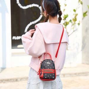 Mini backpack with bow print and red trim, worn as a stylish crossbody bag for women