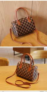 Detailed side view of a brown checkerboard cylinder bag with letter patterns and top handles