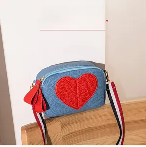 Detail of blue pebbled leather crossbody bag with heart patch and striped strap