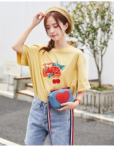 Detail view of blue heart crossbody bag with striped shoulder strap worn on a yellow shirt