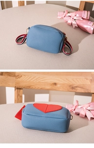 Close-up of blue lychee leather camera bag featuring a red heart and striped shoulder strap