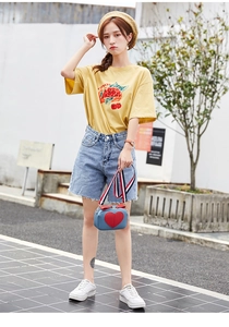 Outdoor street style featuring a yellow graphic tee with a heart-accented blue crossbody bag