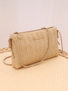 Close-up of woven straw texture with a gold metal logo on a minimalist summer crossbody bag