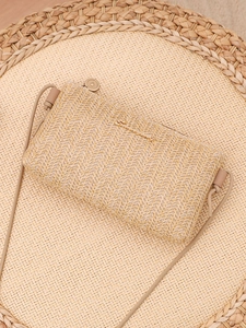 Detailed view of beige woven crossbody bag with metal logo and zipper on texture mat