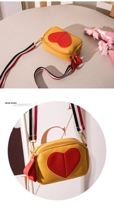 Detail of yellow lychee leather shoulder bag with red heart patch and striped strap