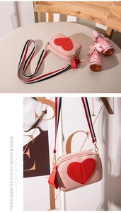 Detail of pink lychee leather crossbody bag with red heart and striped webbing strap