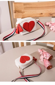 Close-up of white pebble leather crossbody bag with red heart patch and striped strap