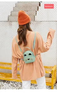 Detail shot of mint green cat-themed mini backpack on model, showing compact size and straps