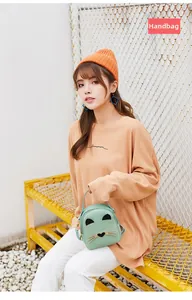 Detail of mint green cat-shaped mini bag with heart nose and gold whiskers on orange sweater