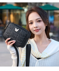 Close-up of black quilted camera bag with white butterfly charm and gold metal hardware
