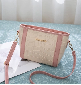 Detail der cremefarbenen Beuteltasche mit Krokoprägung, rosa Gurt und Sunnycity-Logo