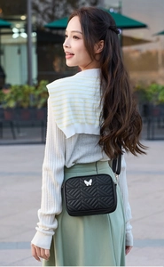 Fashionable black quilted camera bag with butterfly detail shown on female model