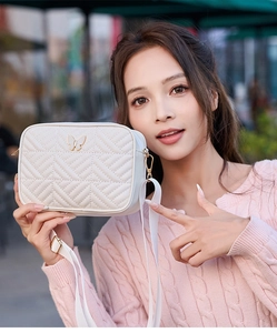 Close-up of white quilted camera bag with golden butterfly logo and wide fabric strap