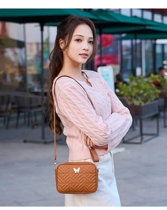 Detail of light brown crossbody camera bag with V-quilted pattern and butterfly buckle