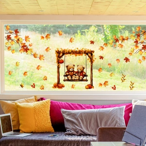 Detail of autumn window decals featuring teddy bears on a swing with orange maple leaves