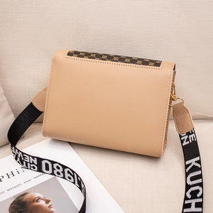 Sac bandoulière beige avec imprimé monogramme et large sangle lettrée sur sofa