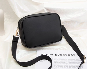 Detail of black crossbody camera bag with wide woven strap and golden metal buckles
