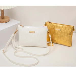 Details von weißen und goldenen Kroko-Handtaschen mit Metallplatten und Schultergurten