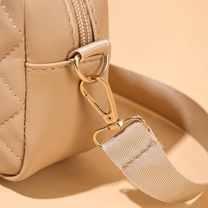Dettaglio dell'anello a D dorato e della trama trapuntata sulla borsa beige a tracolla