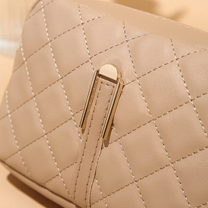 Dettaglio borsa a tracolla trapuntata beige con cuciture a rombi e chiusura in oro lucido