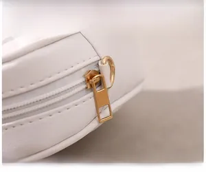Close-up of white leather shell bag featuring smooth gold zipper and metallic D-ring details