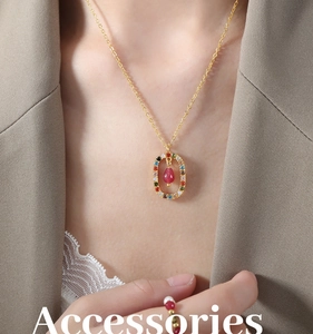 Detail of gold necklace with multicolor stones and red droplet pendant on model