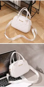 Detailed view of white quilted shell bag with gold logo on a laptop and wooden floor