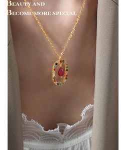 Close-up of a gold oval pendant necklace with red teardrop stone on a model wearing beige