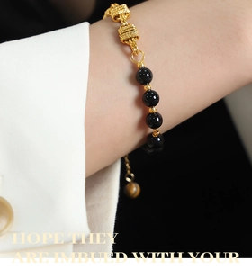 Close-up of gold chain knot bracelet with black agate beads and adjustable tiger eye charm