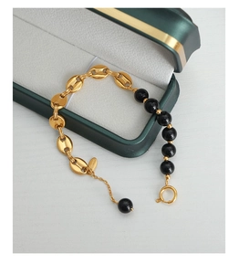 Detail of gold coffee bean chain and black agate beads on a stainless steel bracelet