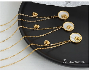 Detail of three gold titanium necklaces featuring white shell daisy pendants on black disc