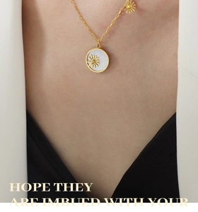 Close-up of gold daisy pendant with white shell inlay worn by model on a gold chain