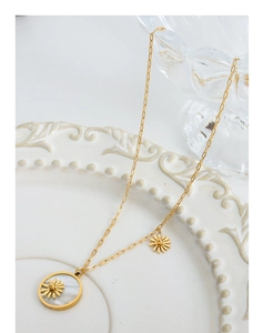 Detail of gold daisy necklace featuring a white shell pendant on a ceramic plate
