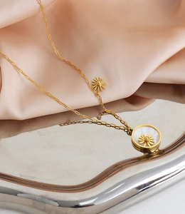 Detail of gold daisy necklace with white shell pendant on a pink satin fabric background