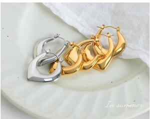 Detail view of gold and silver U-shaped hoop earrings on a textured ceramic plate
