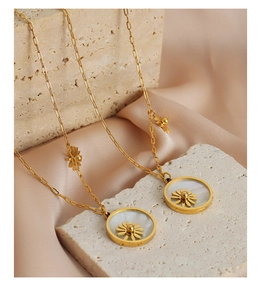 Close-up of gold sunflower shell pendant with paperclip chain on beige stone