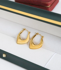 Close-up of chunky gold U-shaped earrings on velvet jewelry box with mirror polish finish
