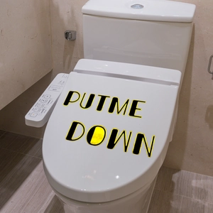 Close-up of Put Me Down slogan sticker with gold foil on a white toilet lid