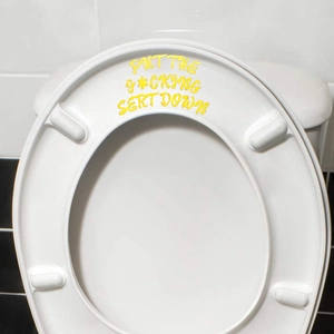 Detail of yellow Put Me Down seat reminder sticker on bathroom toilet lid