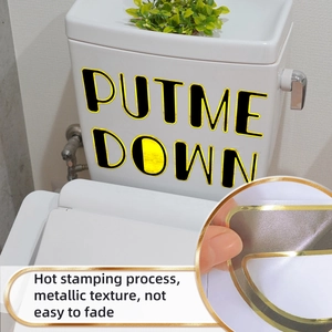 Detail of gold foil 'PUT ME DOWN' toilet seat sticker with metallic texture and finish
